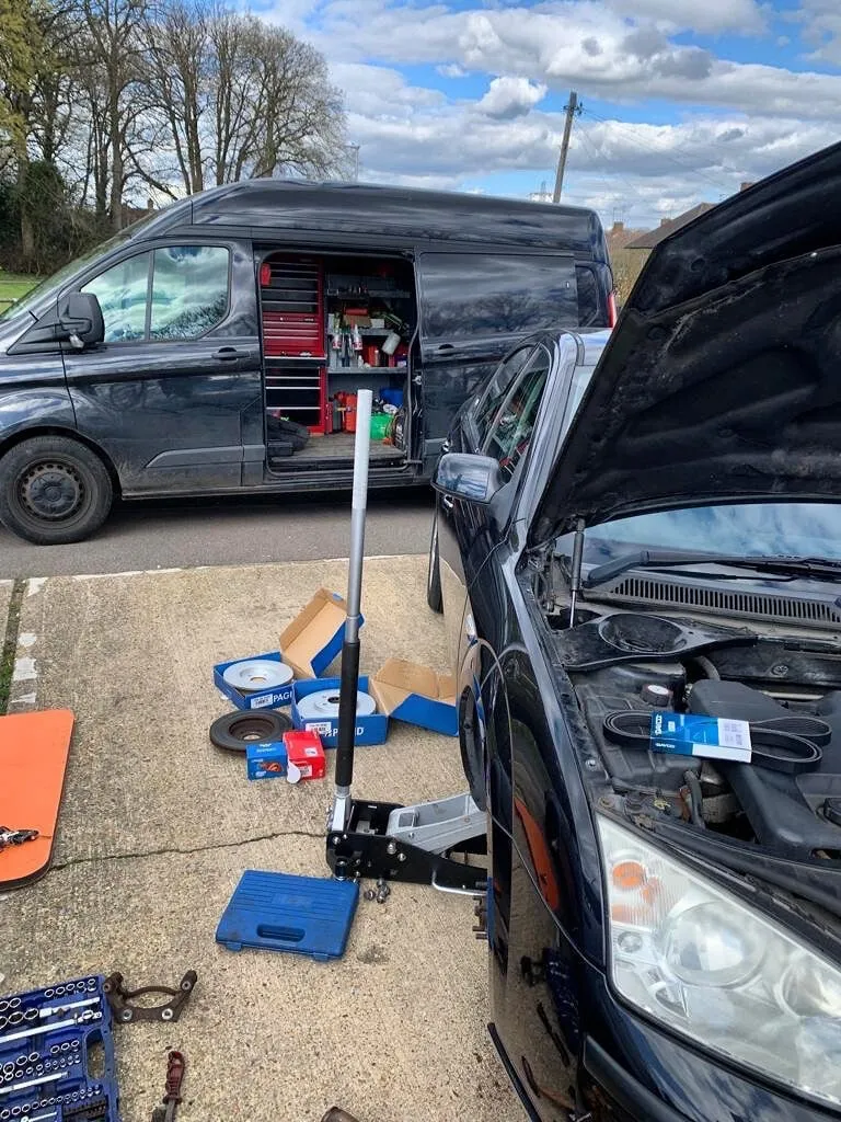 Our van parked beside a car mid brake job, with new discs and pads laid out on the driveway
